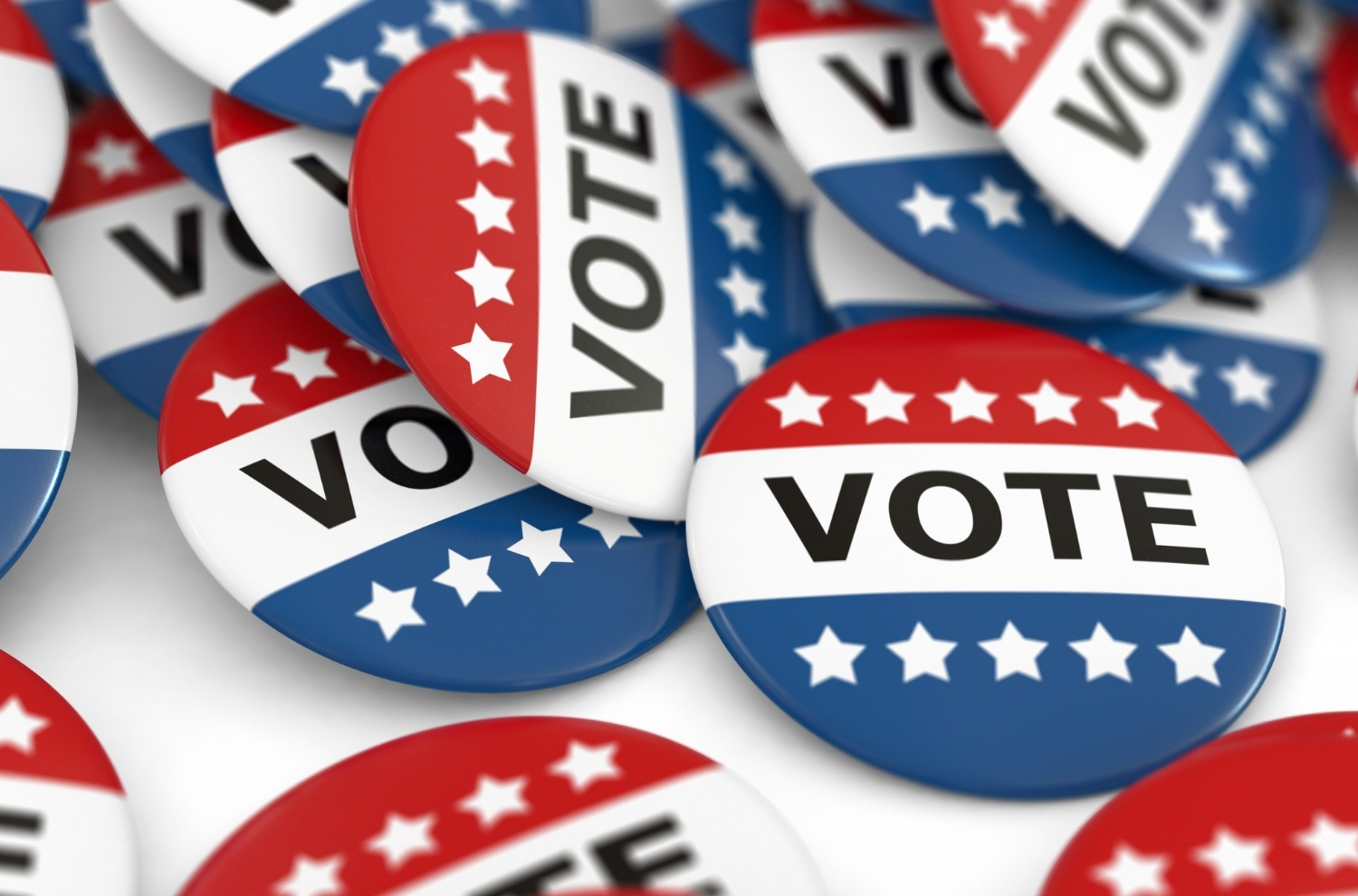 Pile of lapel pins that say "vote" with red and white stripes sitting atop a white table.