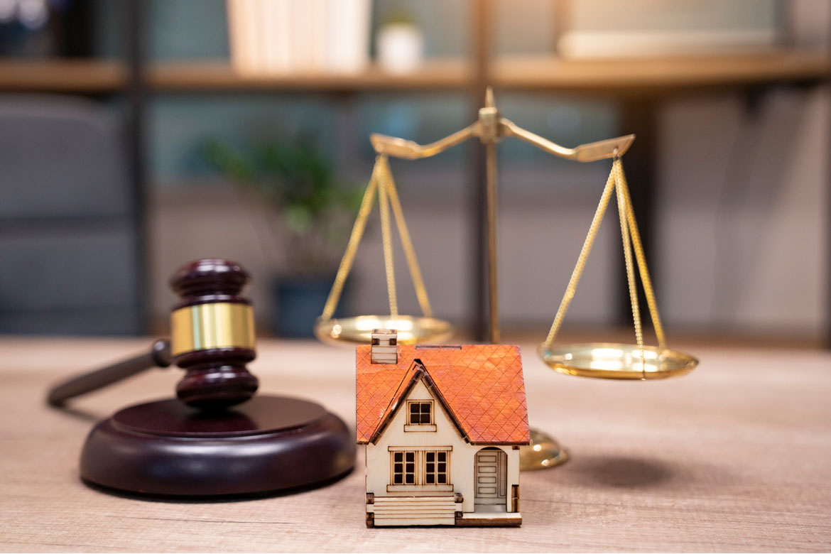 Model of house sitting on desk next to gavel and legal scales.