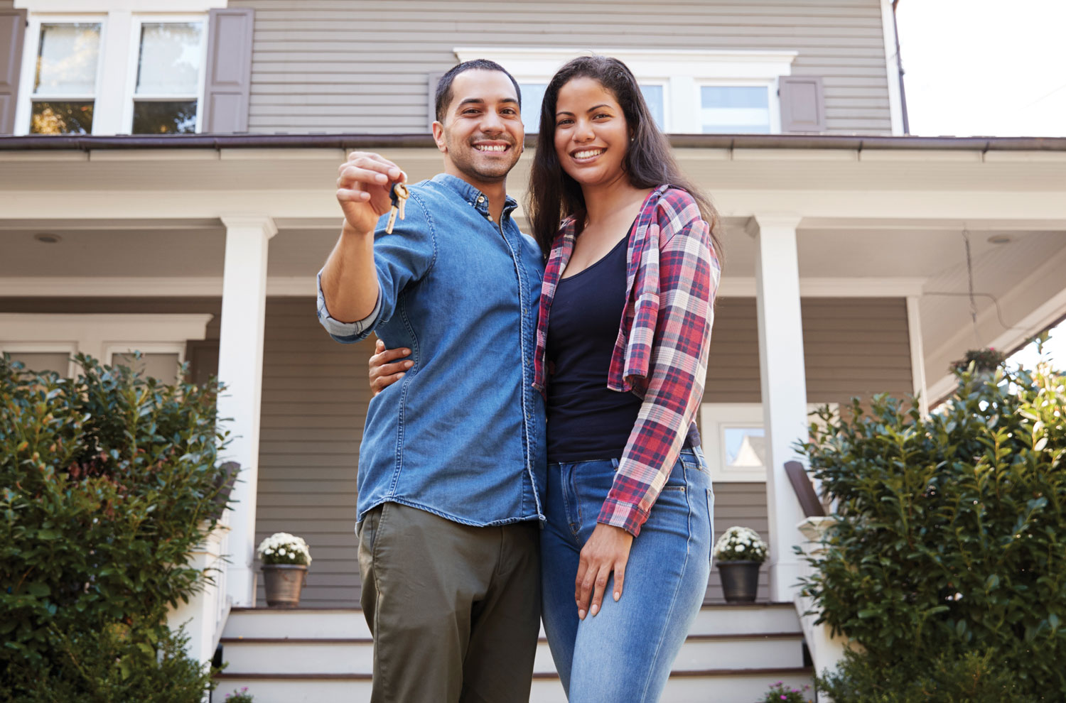 Couple holding house key in front yard of home