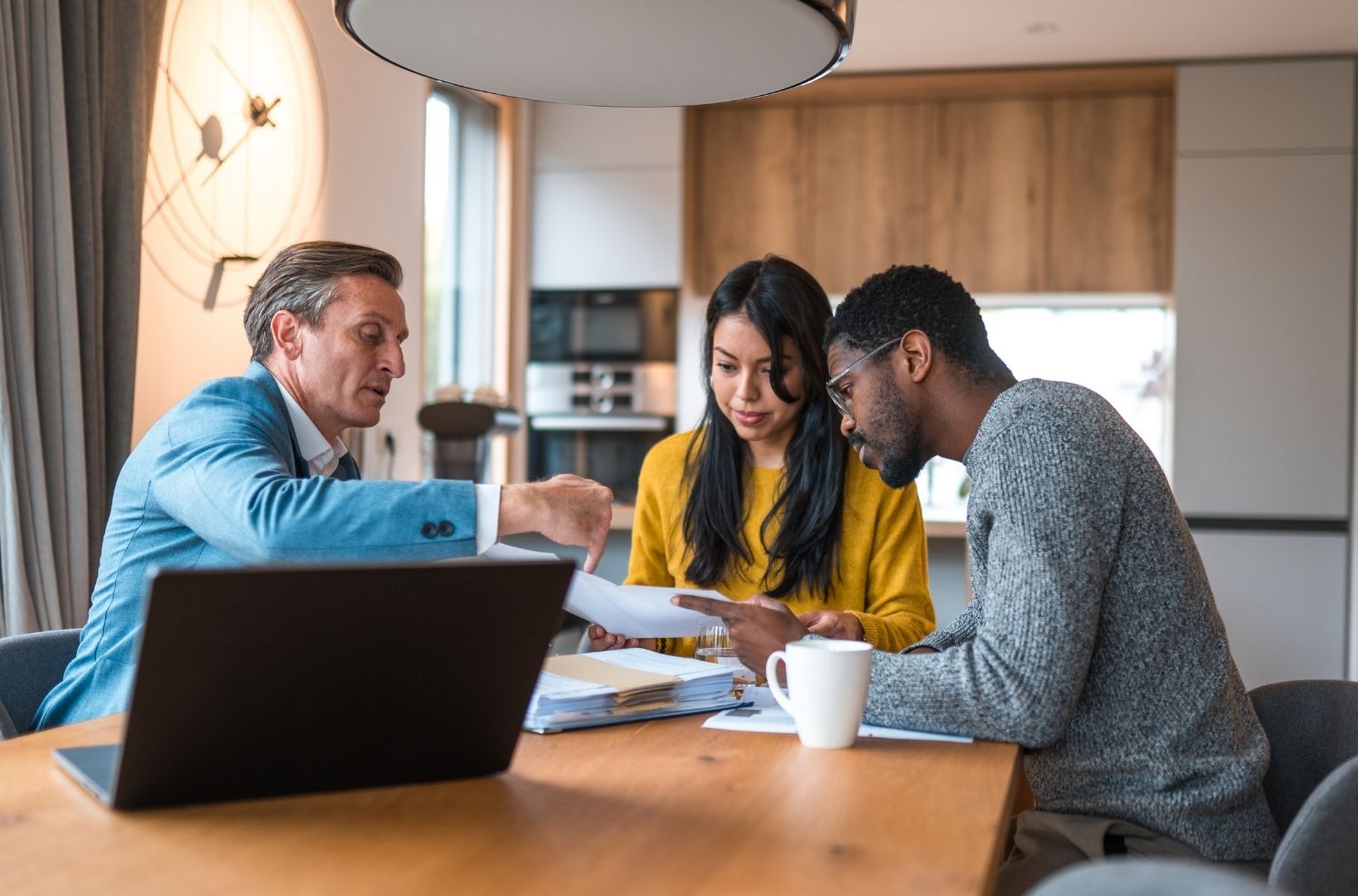 Male real estate agent discussing paperwork with couple sitting at kitchen table
