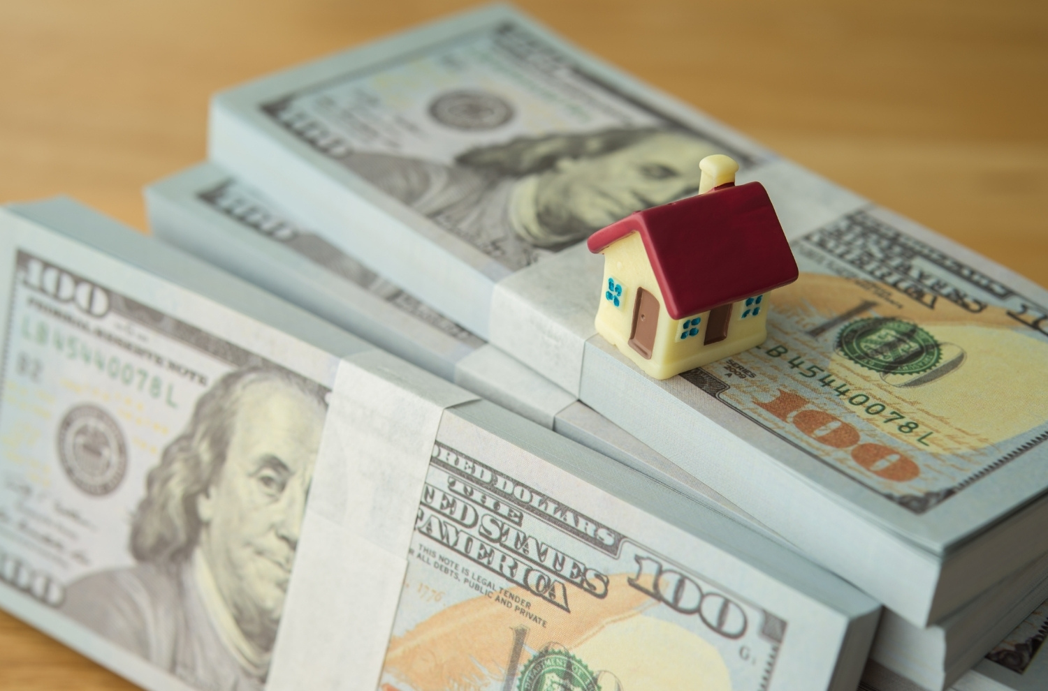 Small model home sitting atop stacks of US dollar bills
