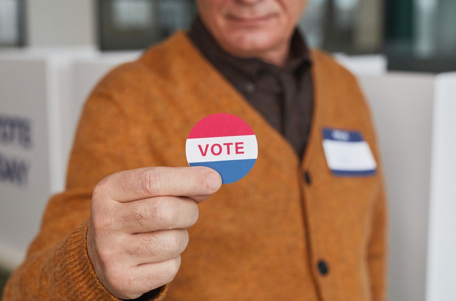 Man holding up circular sticker that says vote