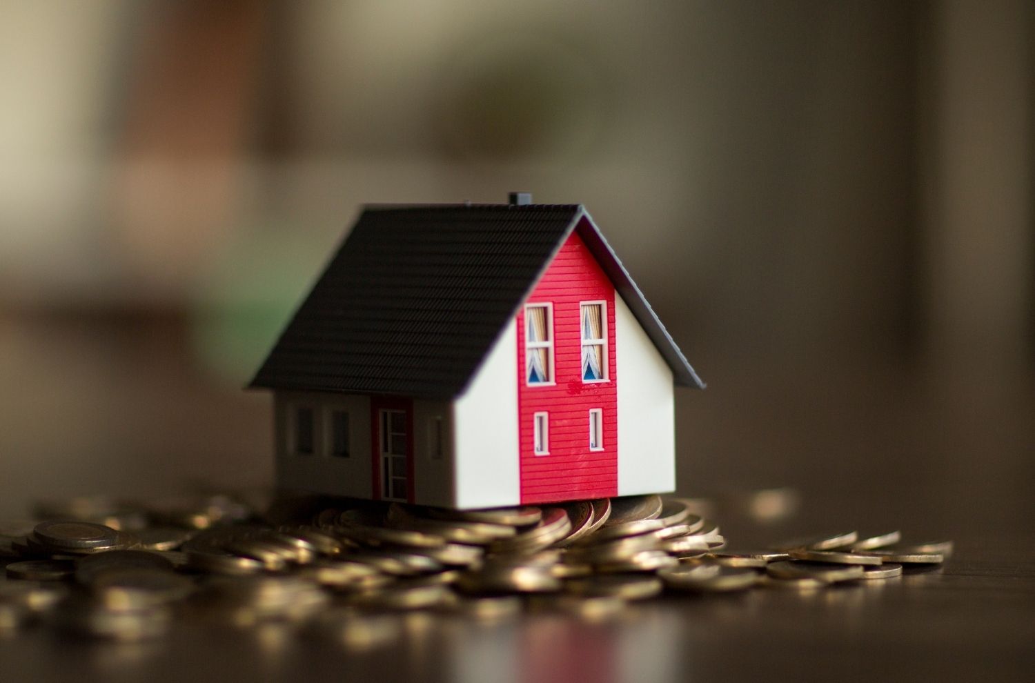 Small model house sitting atop coins and money